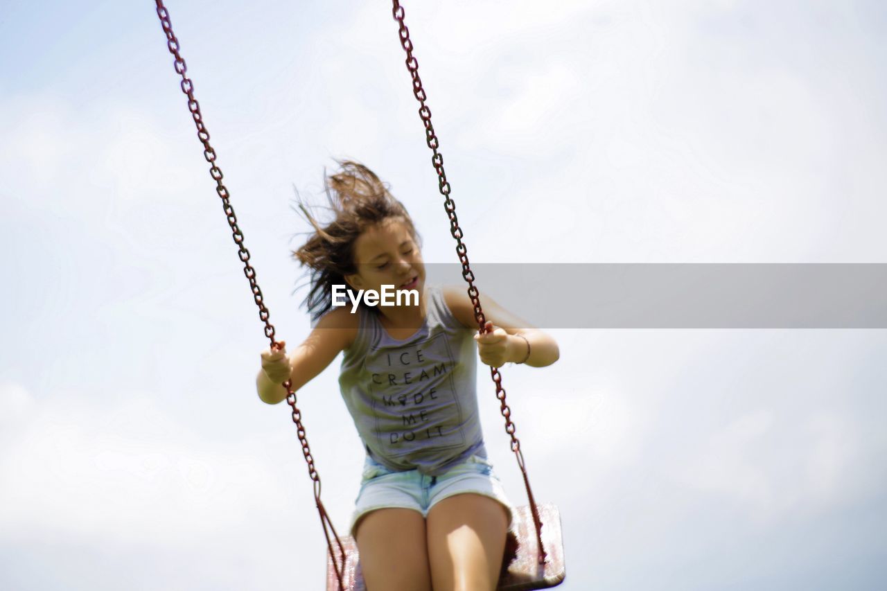 Low angle view of girl on swing against cloudy sky