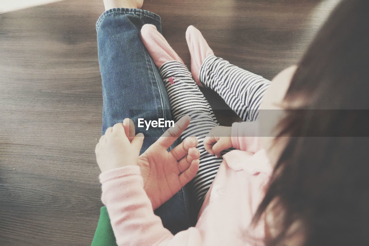 Low section of mother and daughter sitting on hardwood floor