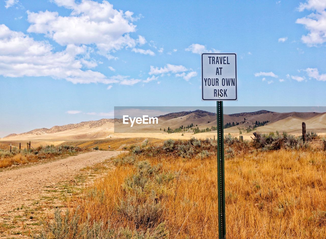 ROAD SIGN ON FIELD BY MOUNTAIN AGAINST SKY