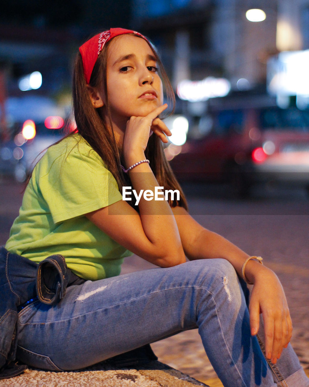 Young woman looking away while sitting on street in city at night