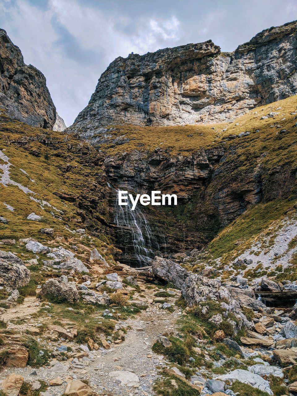 Scenic view of rocky mountains and waterfall against sky