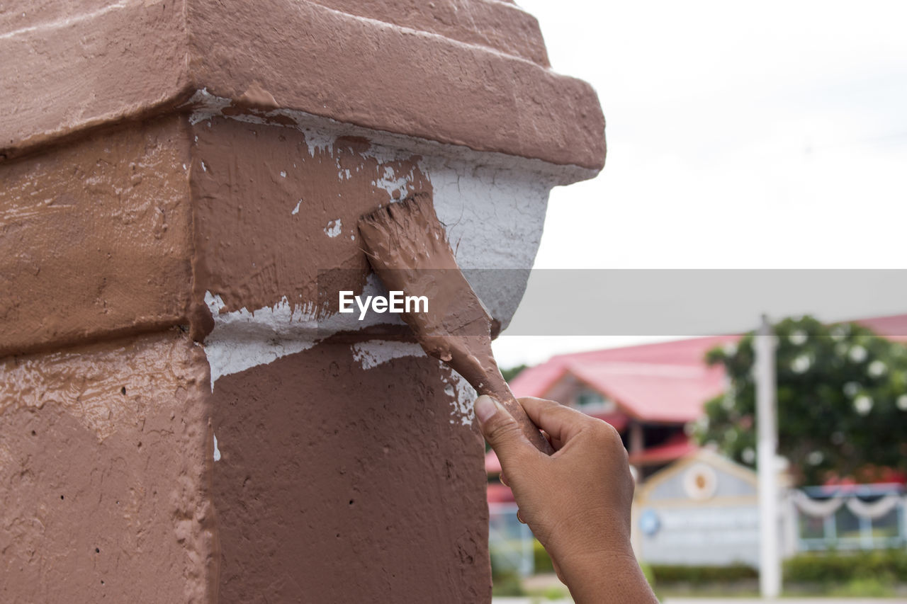 Cropped hand of male painter painting brown paint on wall