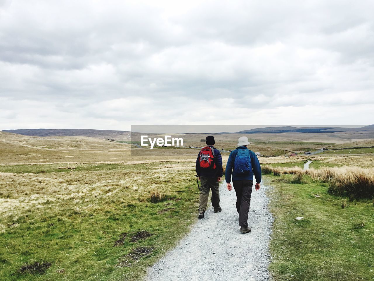 Rear view full length of people walking amidst field on road