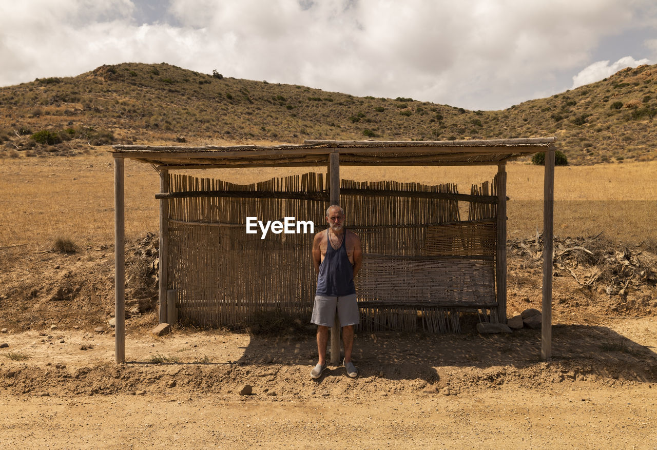 Full length portrait of adult man waiting bus in a wooden bus stand in nature park in summer