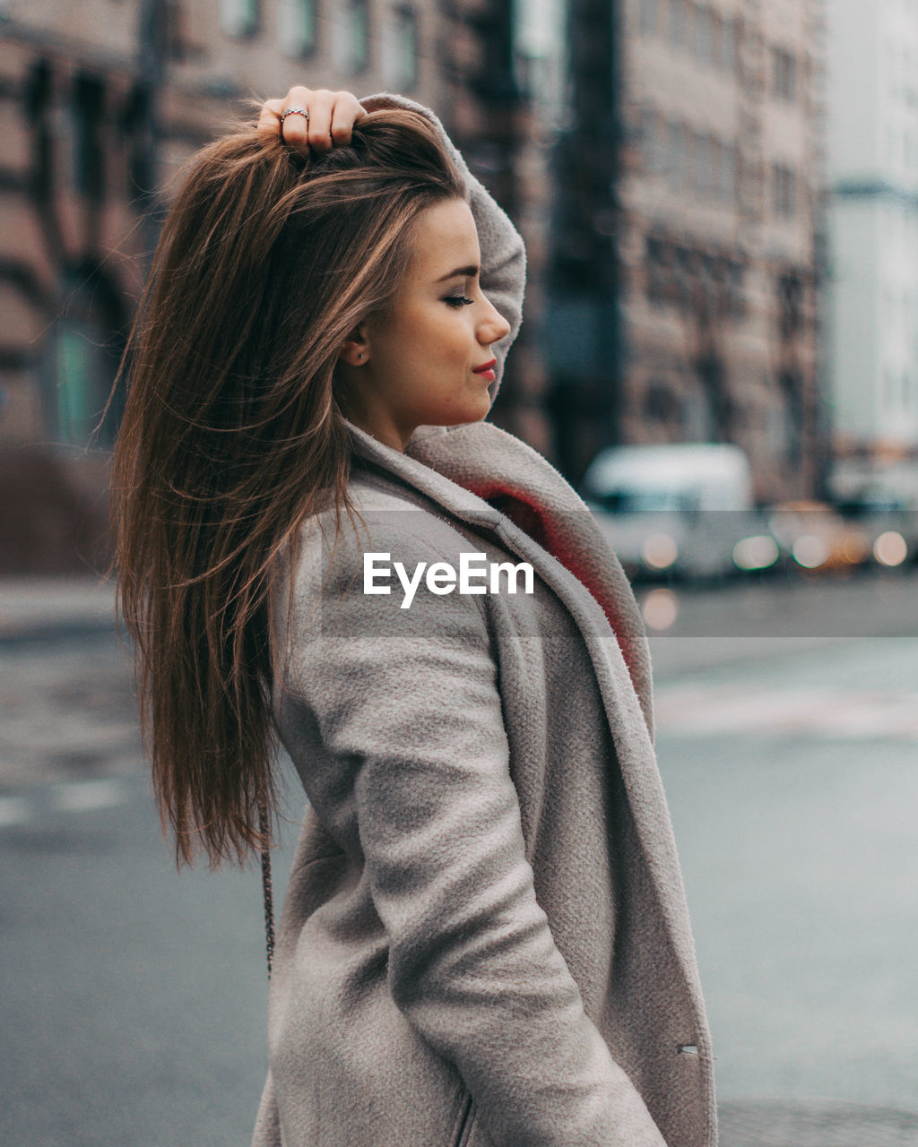 SIDE VIEW OF YOUNG WOMAN LOOKING AWAY WHILE STANDING ON STREET