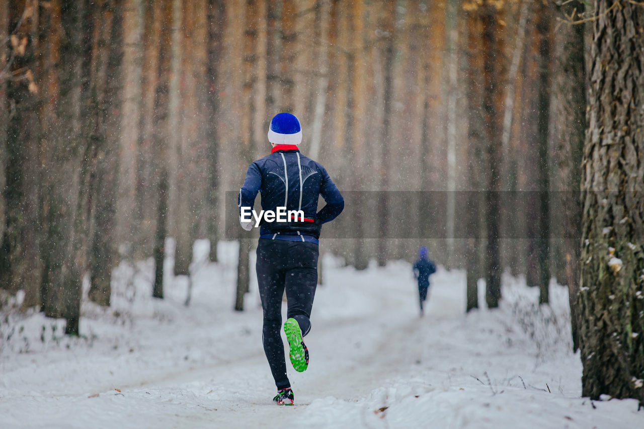 Male runner run winter race in forest on snowfall