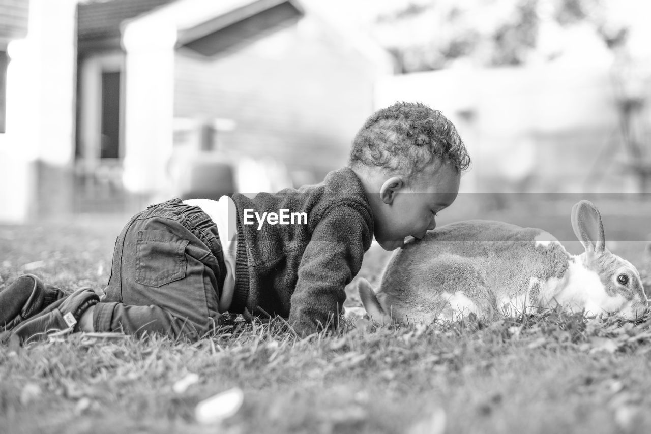 Baby boy kissing rabbit while kneeling on grass