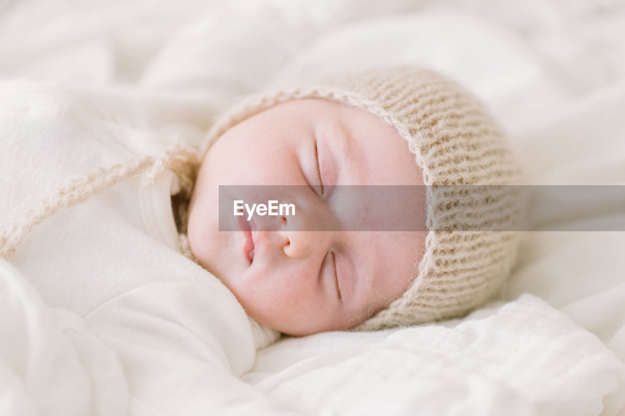 Newborn baby in knit bonnet sleeping on white bed