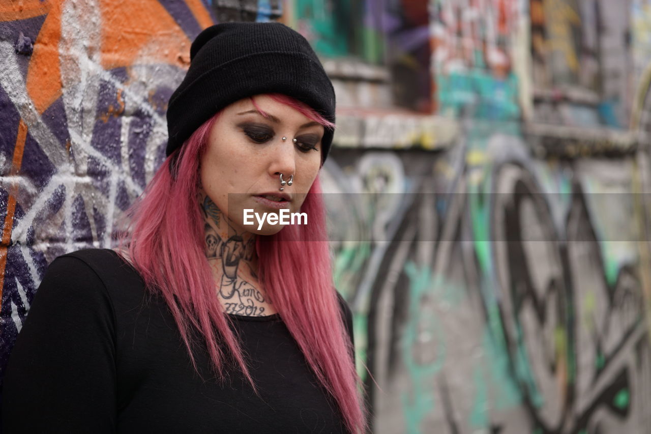 Young woman with pink hair standing against graffiti wall