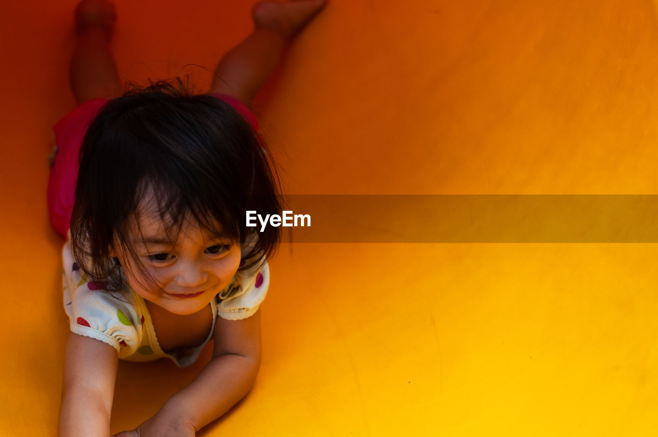 High angle view of cute girl lying on yellow slide