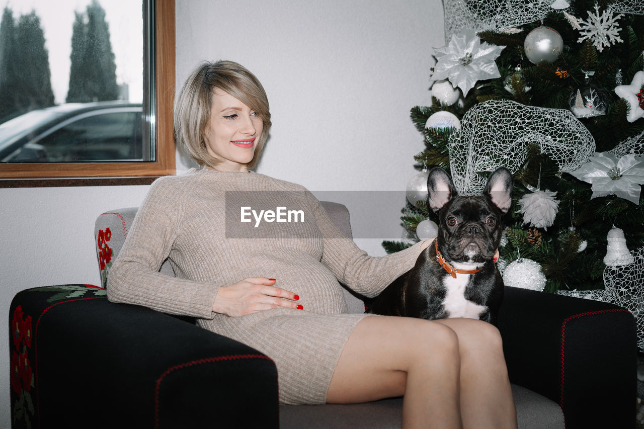Portrait of woman and dog sitting by christmas tree