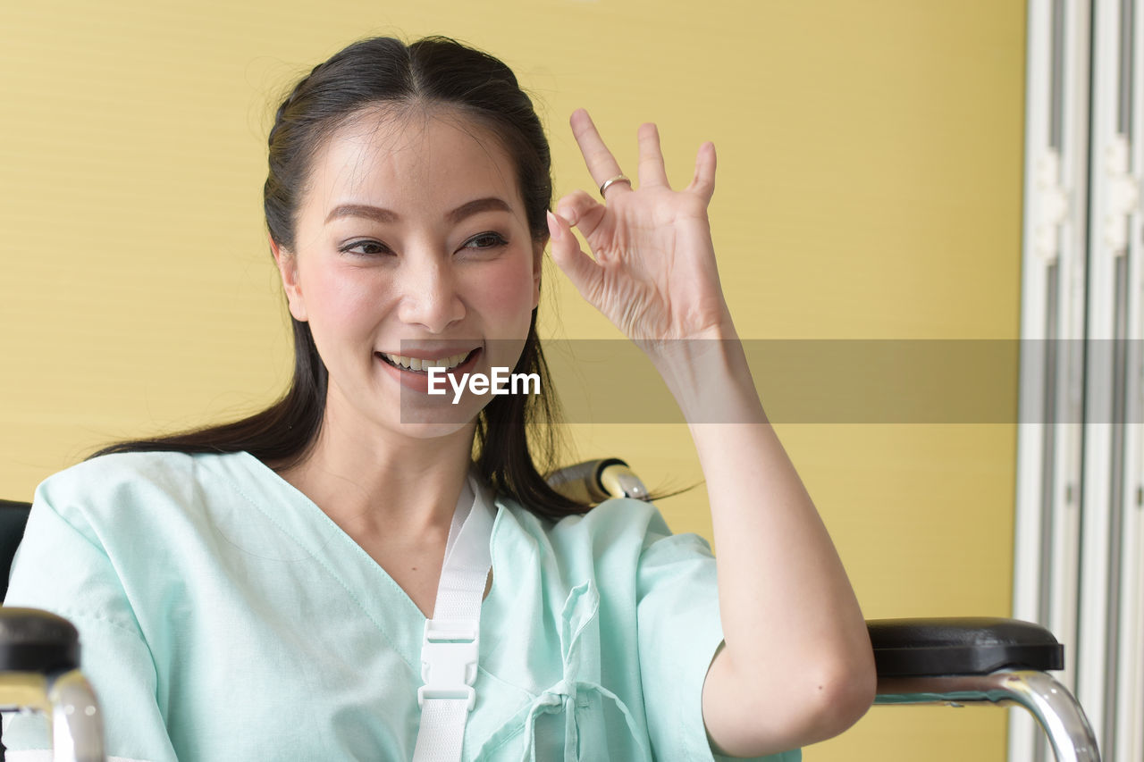 Smiling disabled woman gesturing while sitting on wheelchair against wall