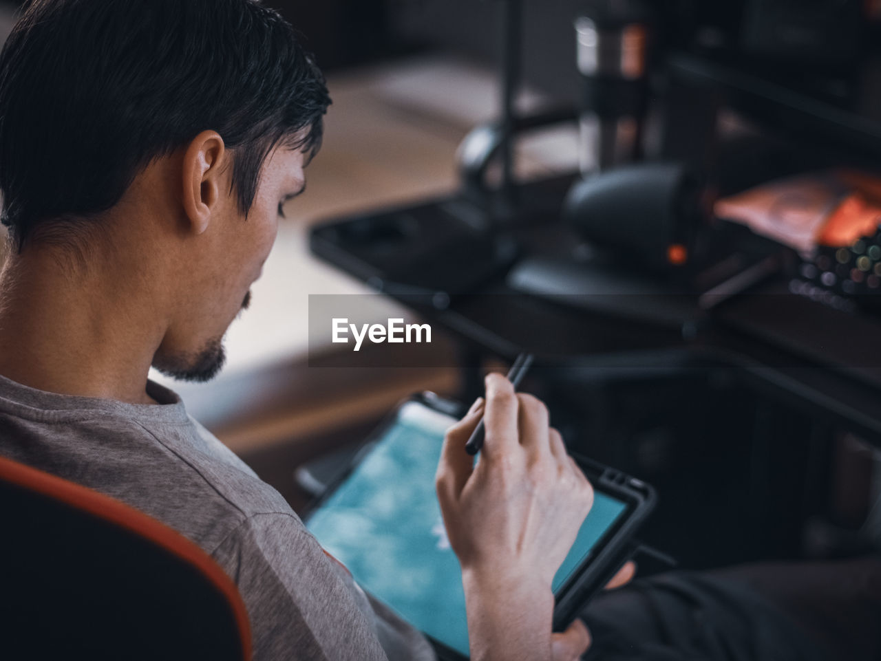 A caucasian guy sits in a work chair and holds a tablet with a black pen on his knees