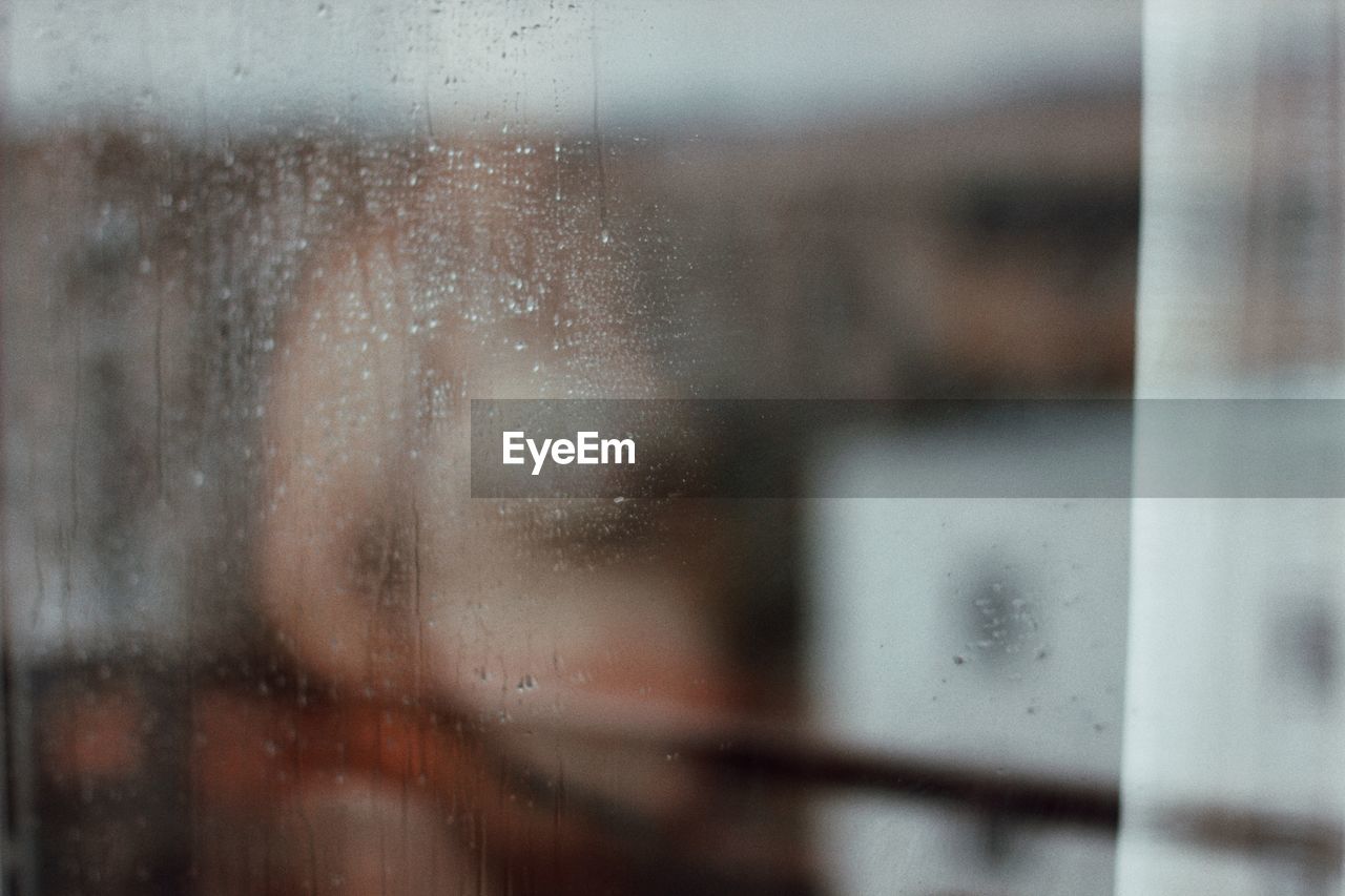 Defocused image of naked woman standing behind wet window