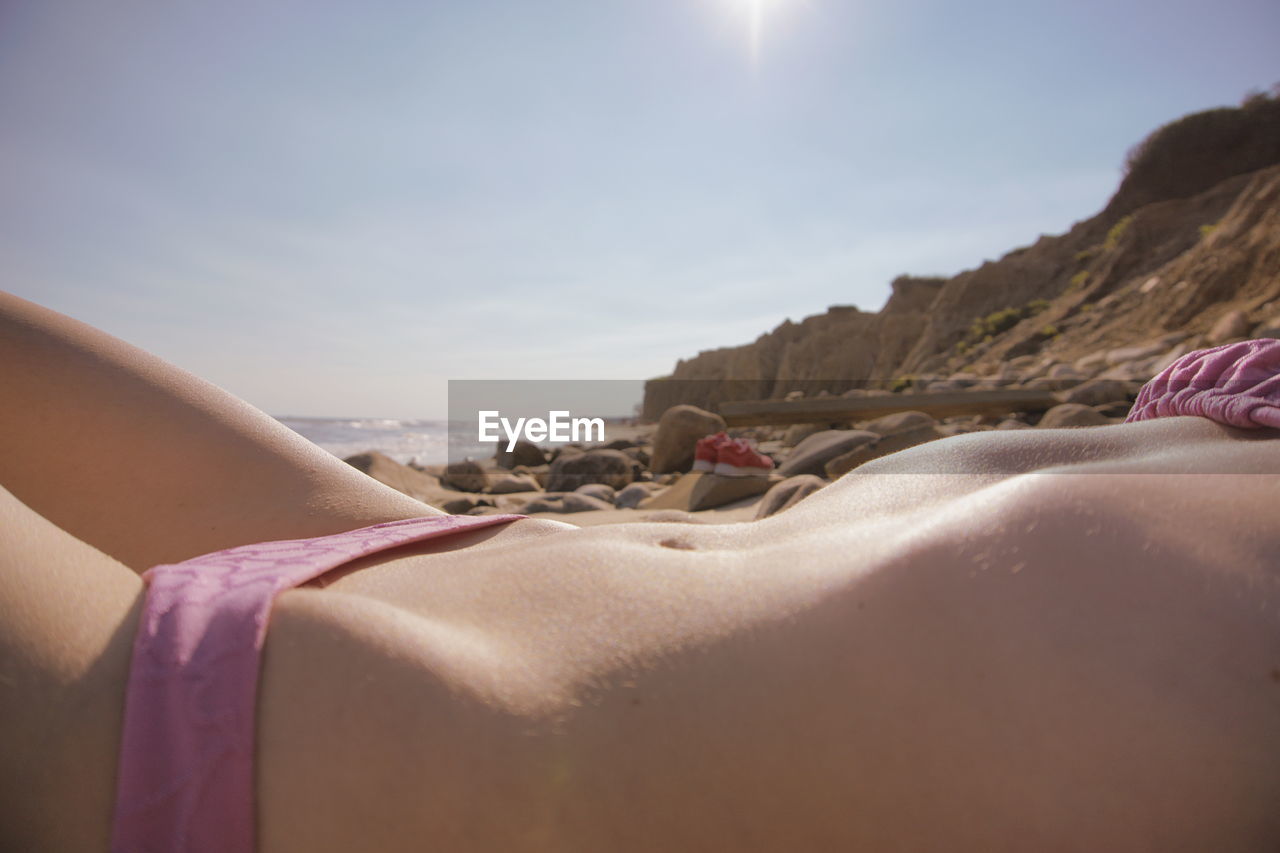 Midsection of young woman in bikini lying at beach during sunny day