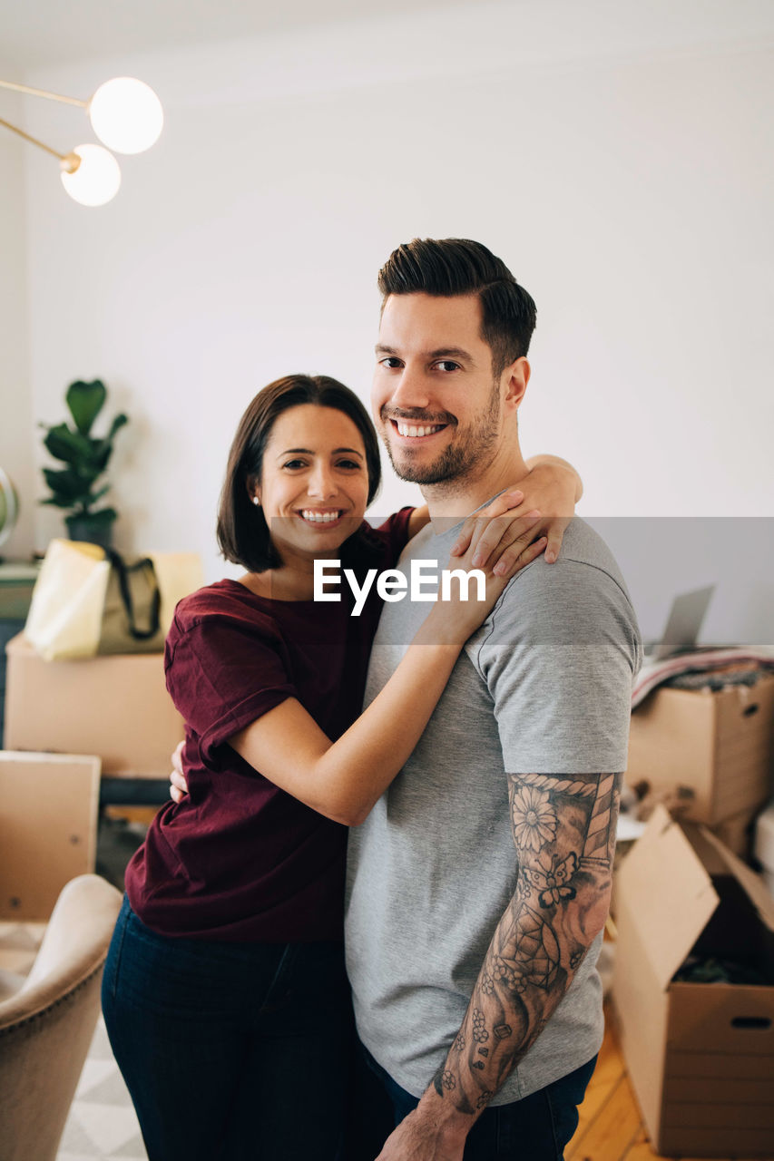Portrait of smiling couple embracing while standing in living room during relocation
