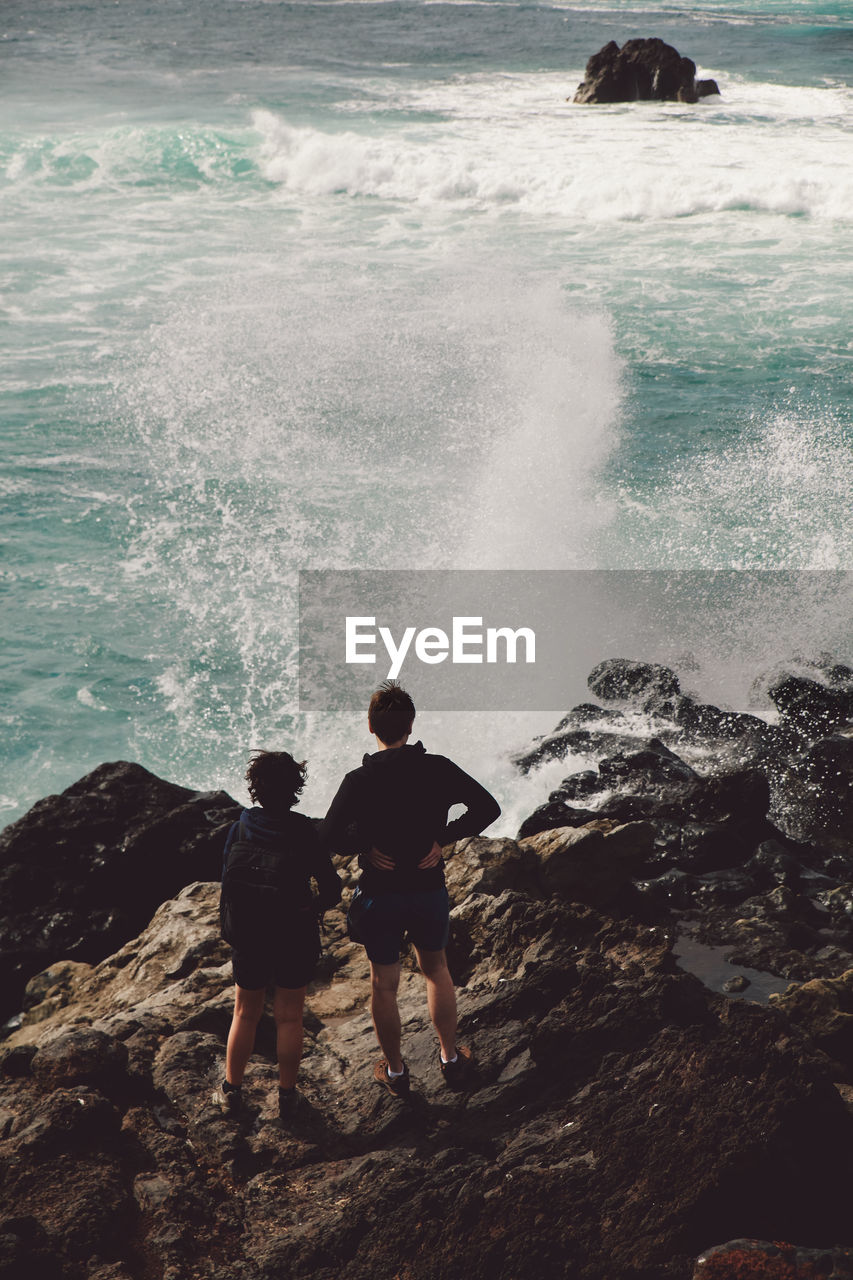 Rear view of couple standing on cliff by sea 