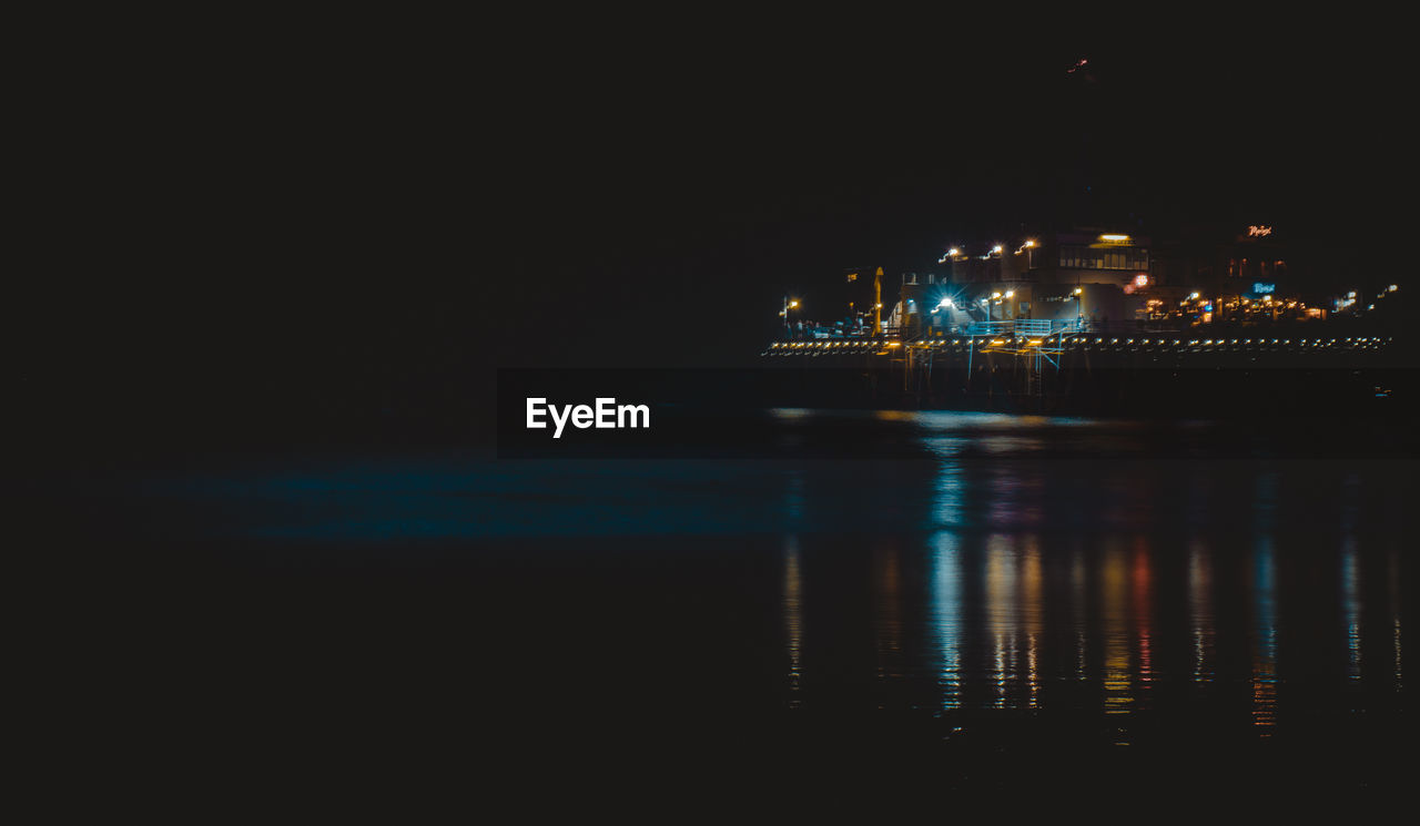 Illuminated city by sea against sky at night