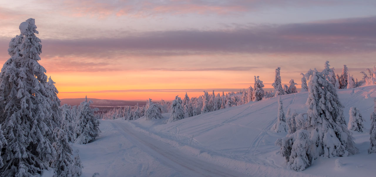 Snow covered landscape against sky during sunset