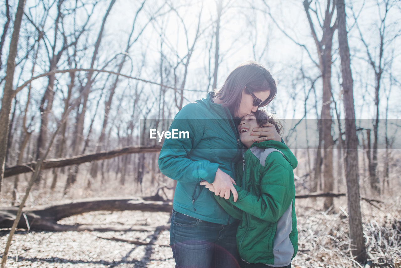 Mother embracing son while standing in forest