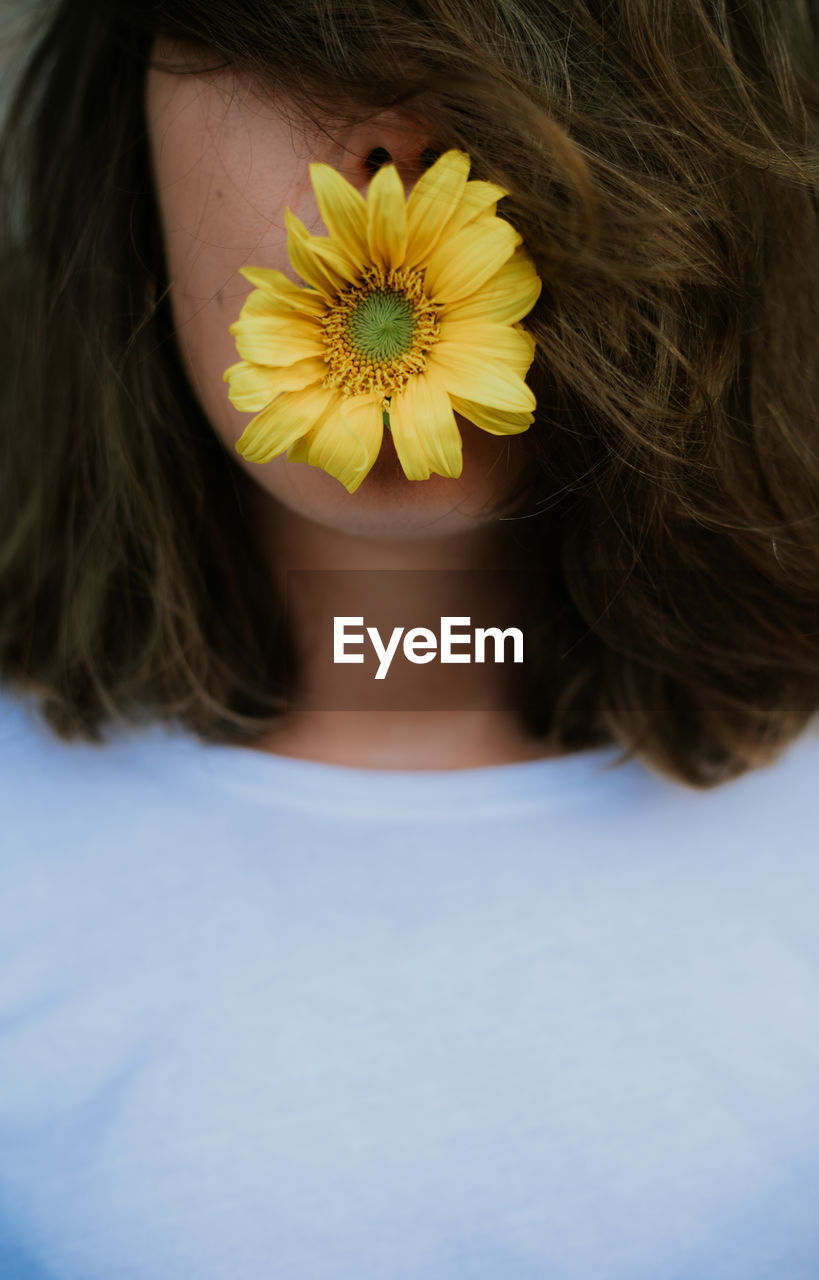 Anonymous woman with hair covering face holding daisy flower in her mouth