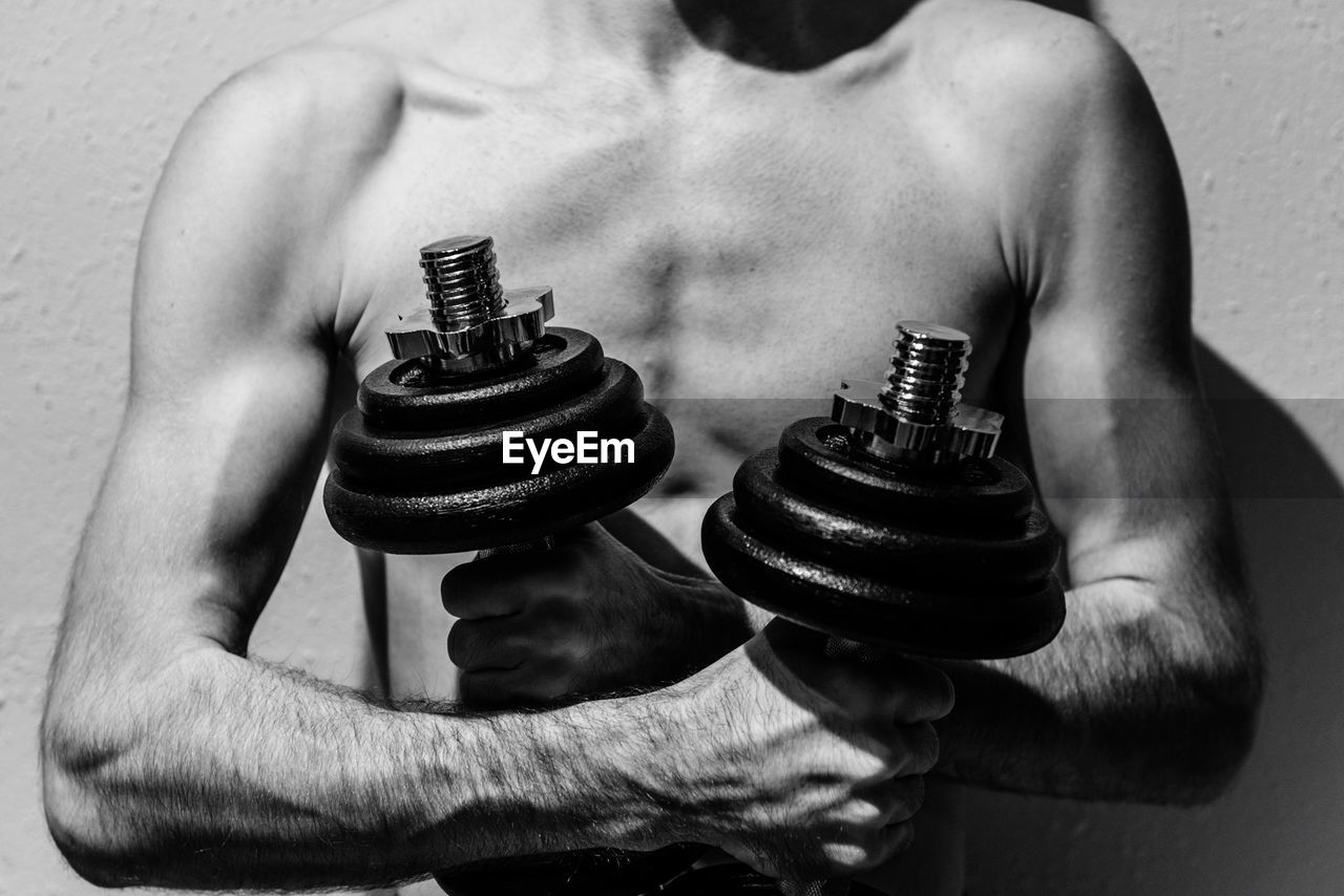 Midsection of shirtless man holding dumbbells