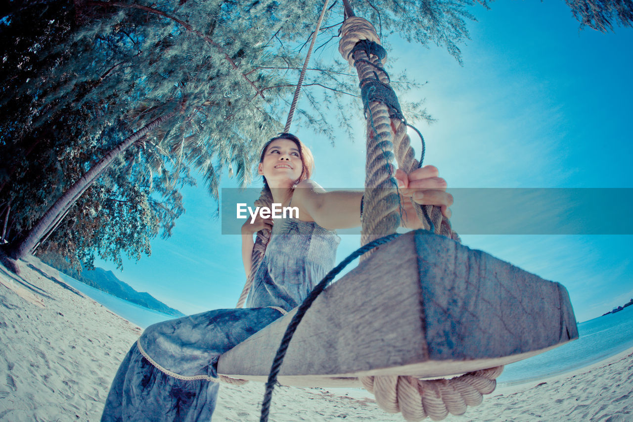 Low angle view of woman sitting on swing at beach