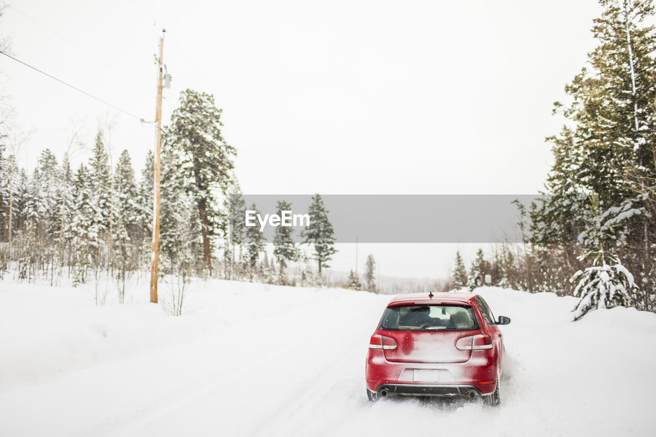 Rear view of red hatchback car driving on snow covered road.