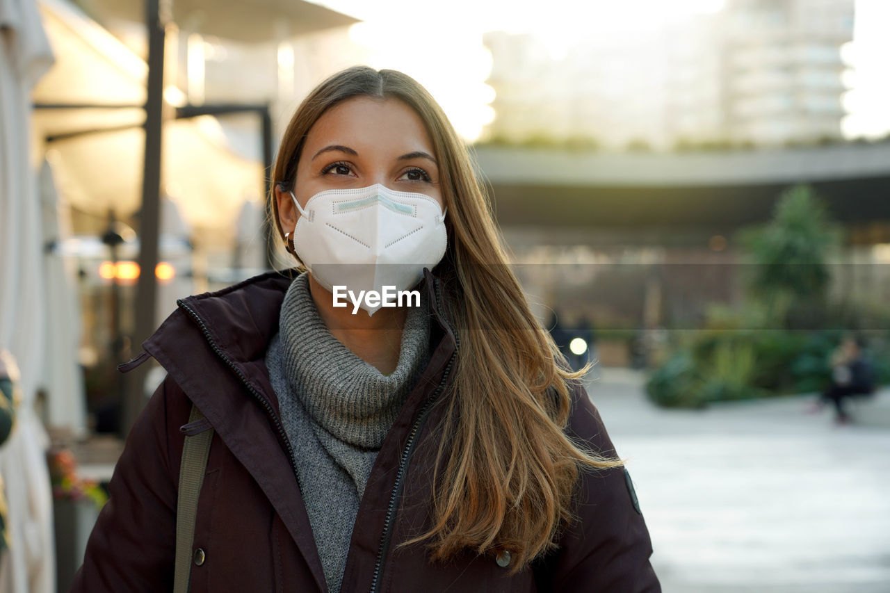 Portrait of young woman wearing medical face mask in city street as prevention against virus