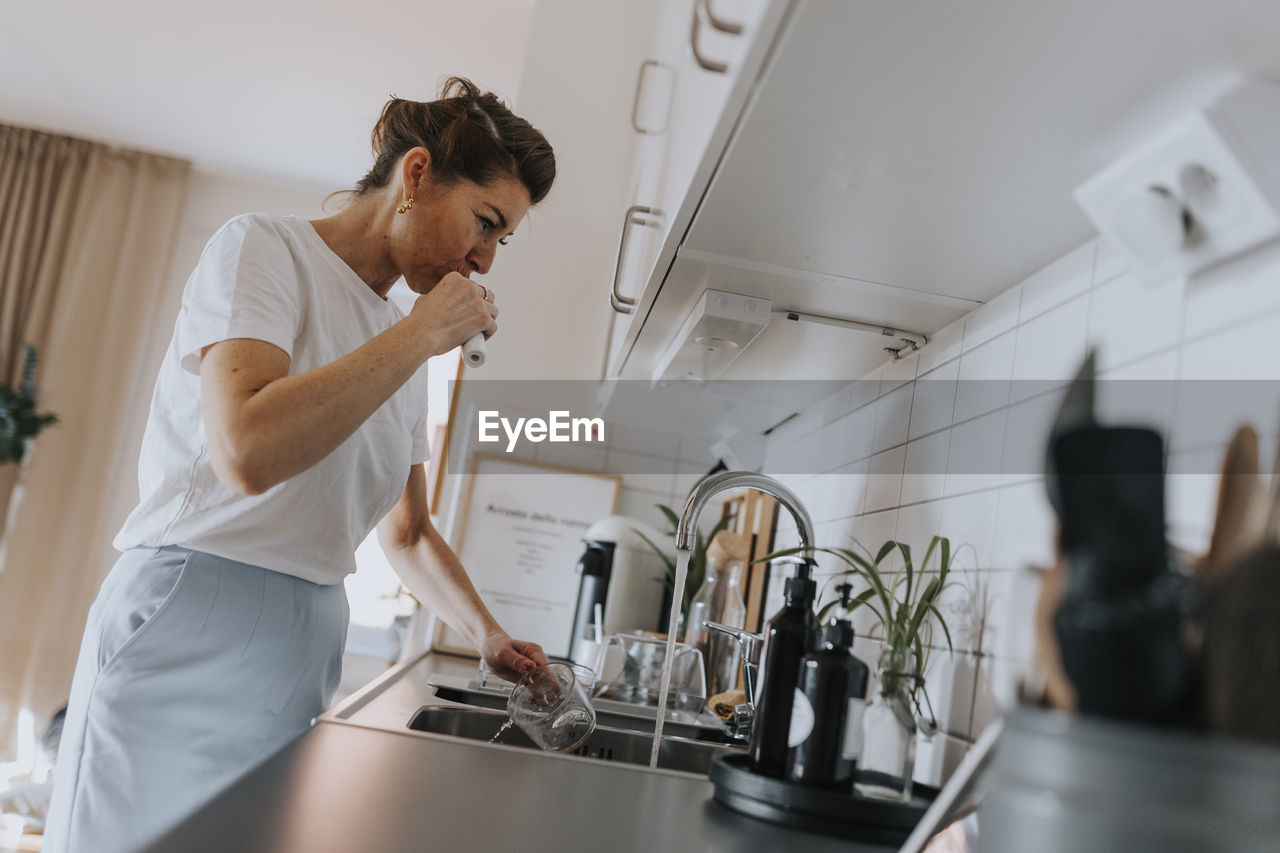 Woman brushing teeth at kitchen sink