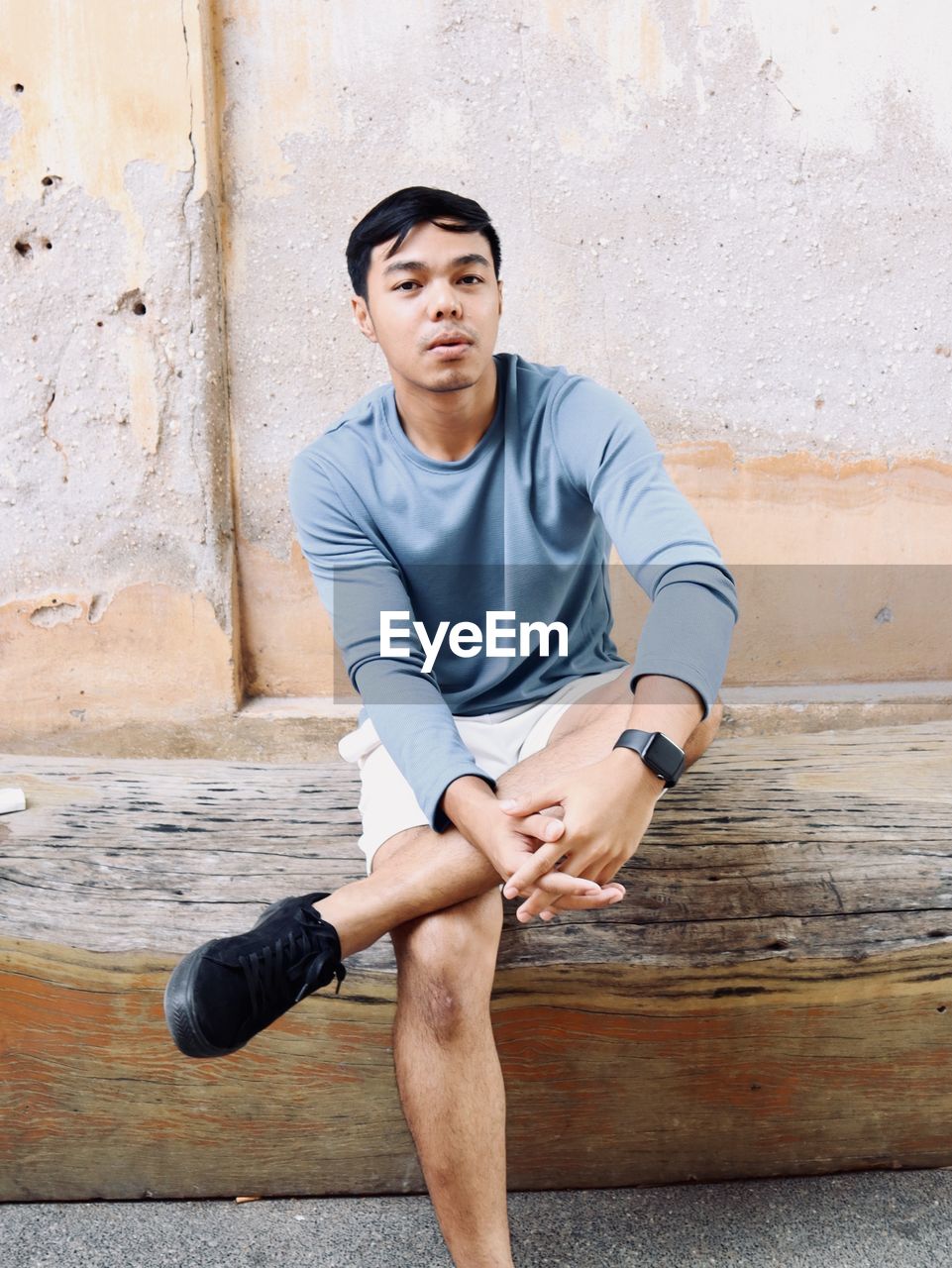 Portrait of young man sitting against wall