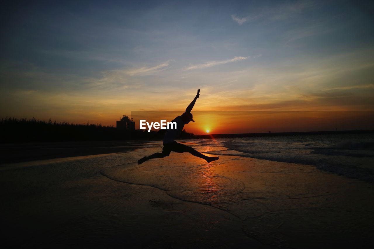 Silhouette man jumping on beach during sunset against sky