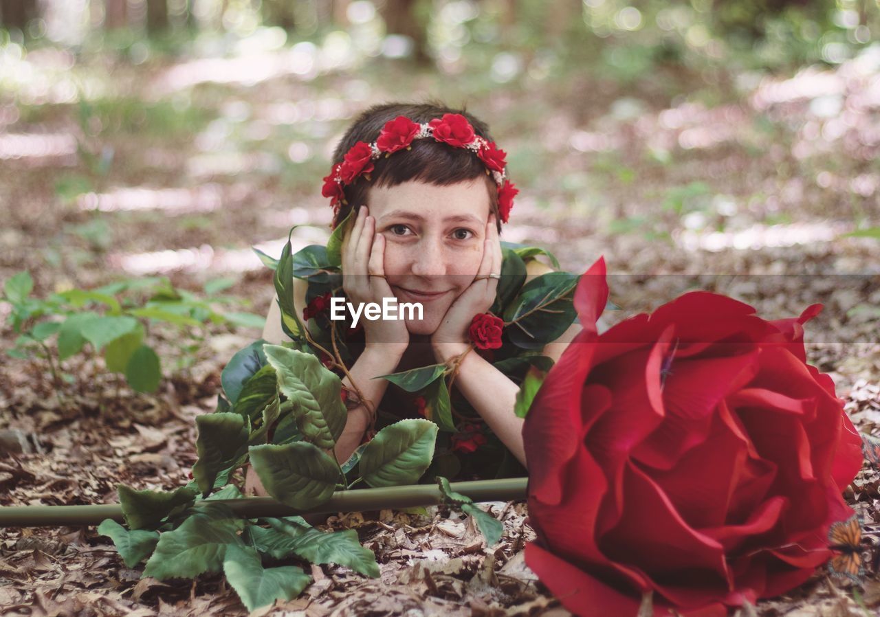 Portrait of smiling young woman with red flowers on land