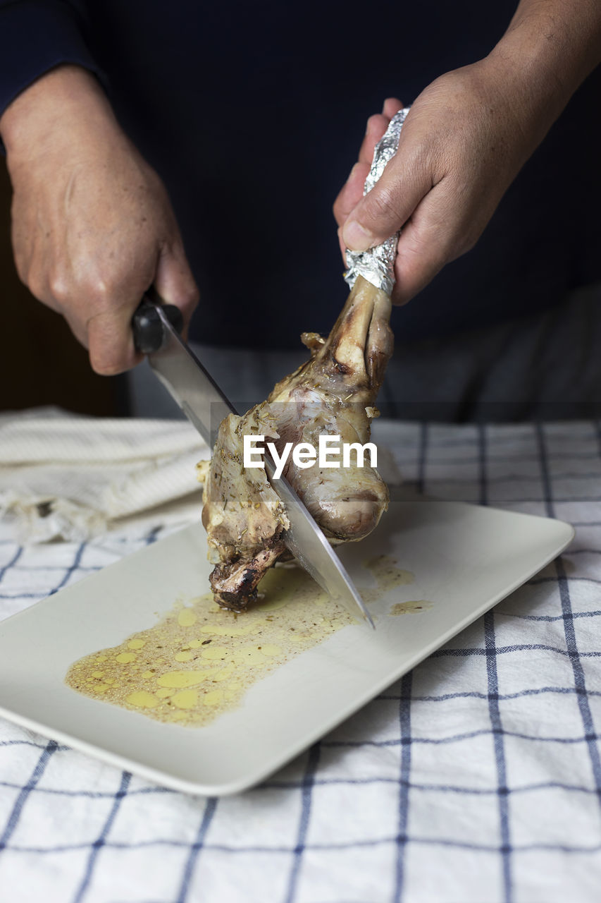 Male hands cutting a baked lamb leg with a knife.