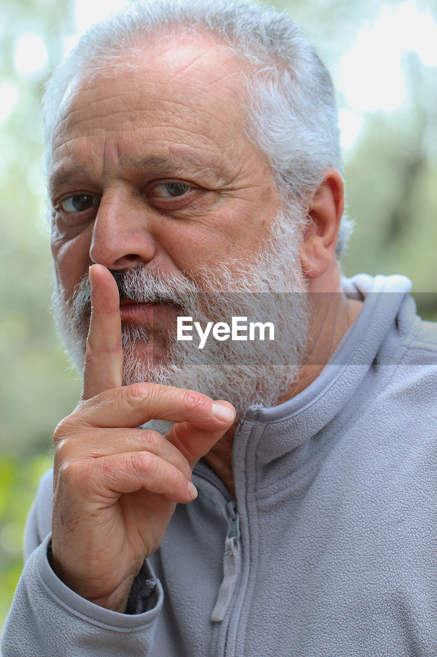 Close-up portrait of senior man with finger on lips