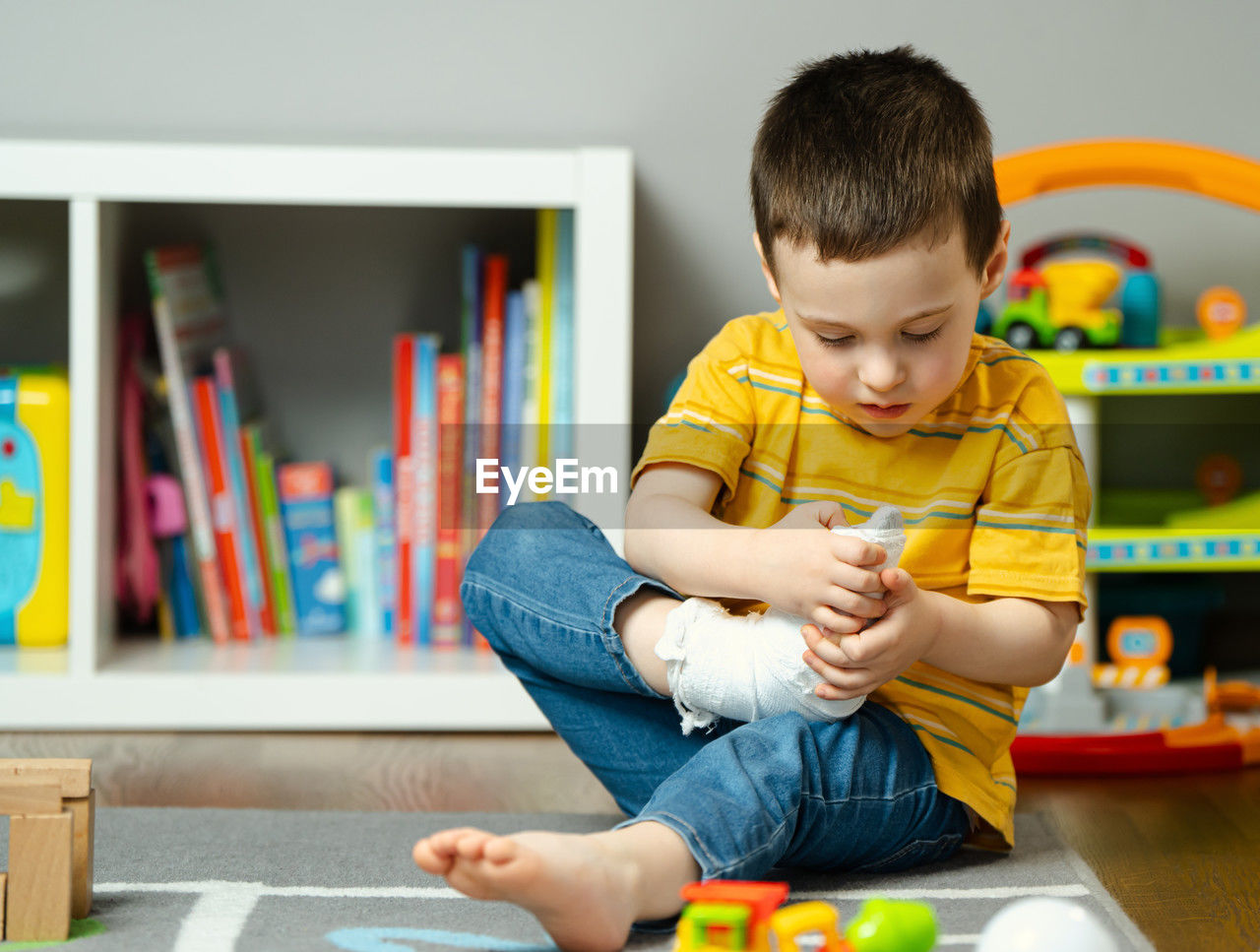 A little toddler boy holds his leg in a cast with his hands. fracture of a foot