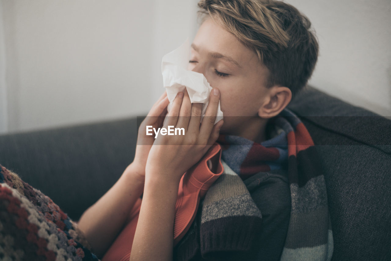 Boy suffering from cold and flu sitting on sofa at home