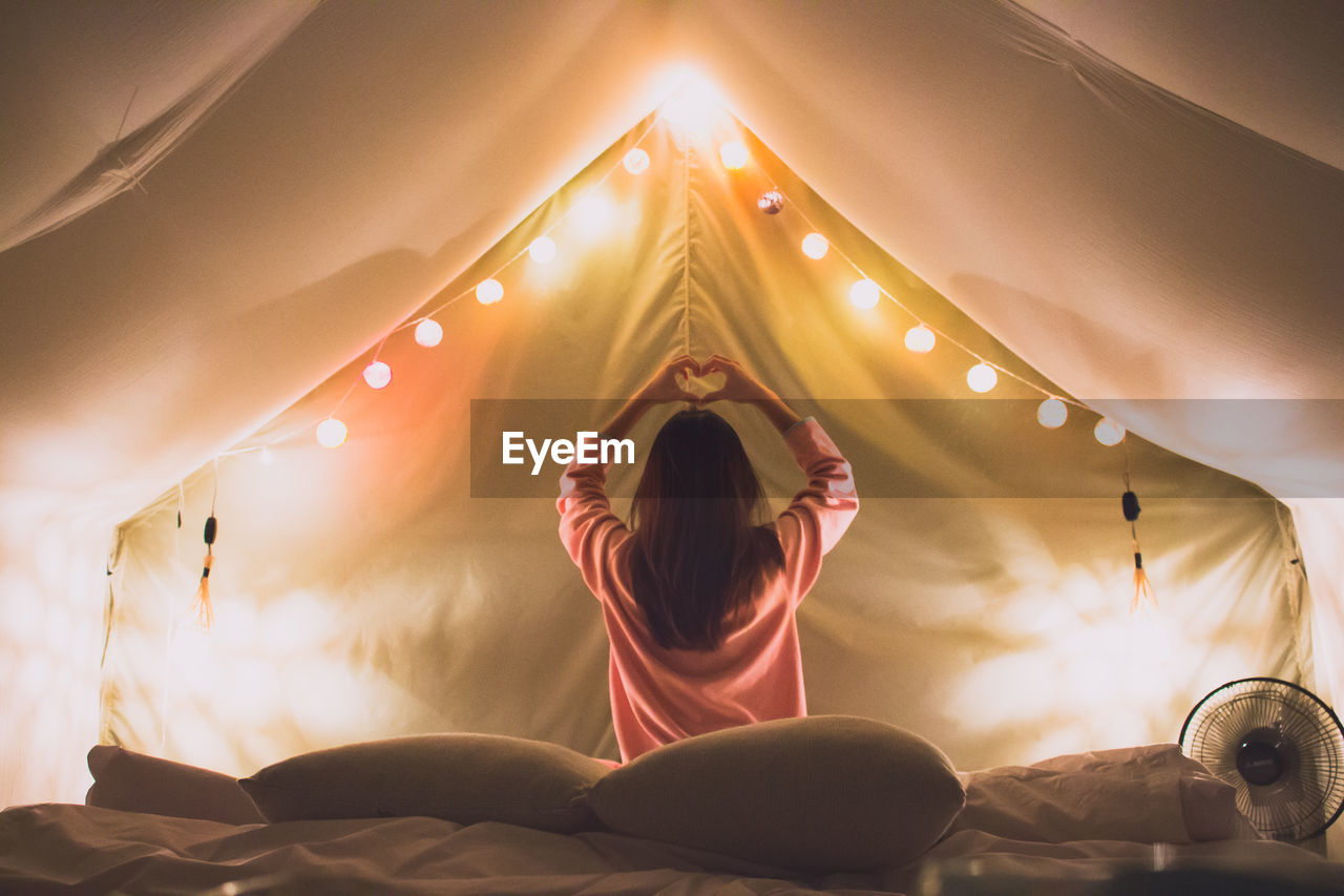 Rear view of woman relaxing on bed in tent