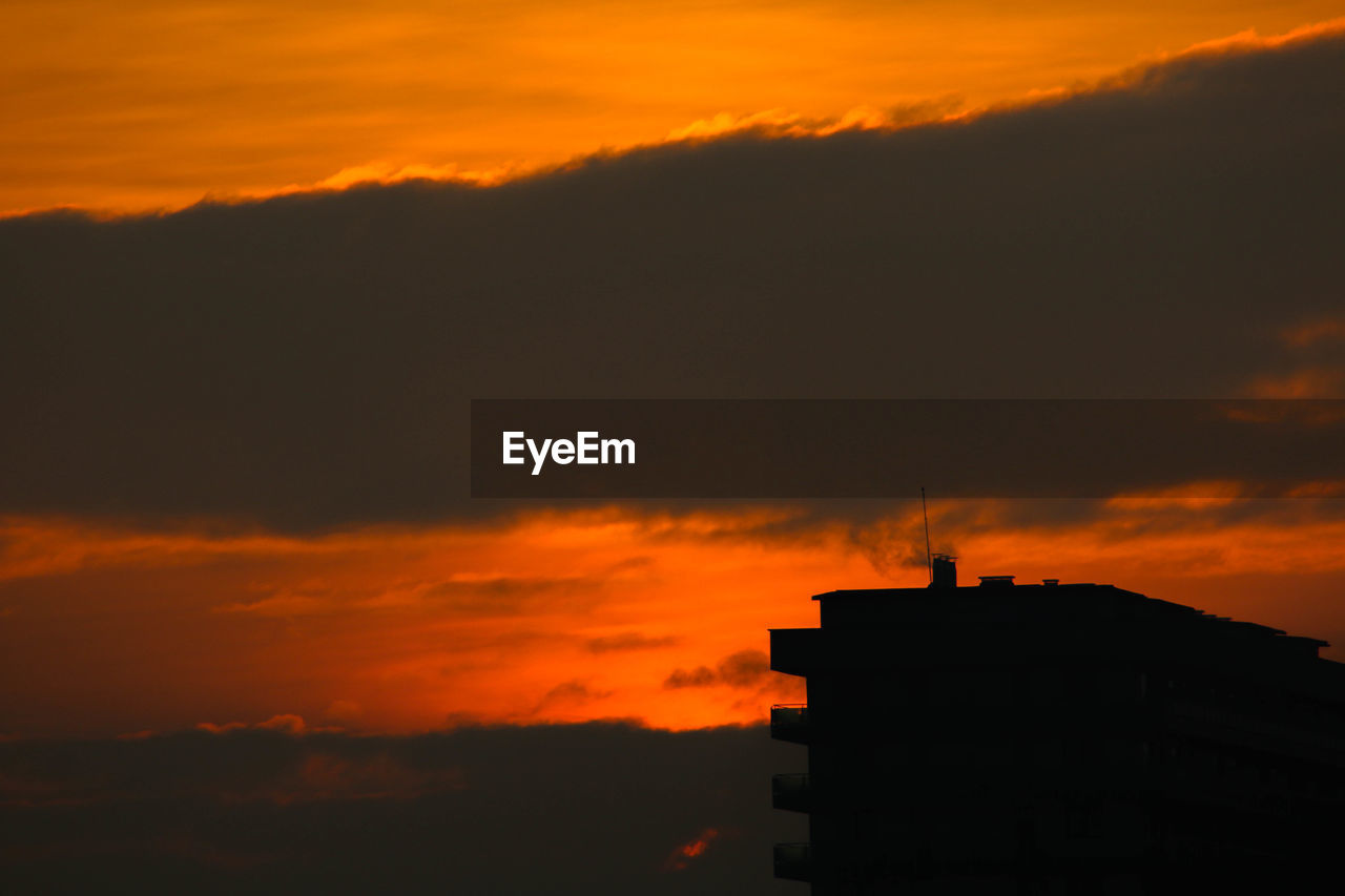 Low angle view of silhouette building against orange sky