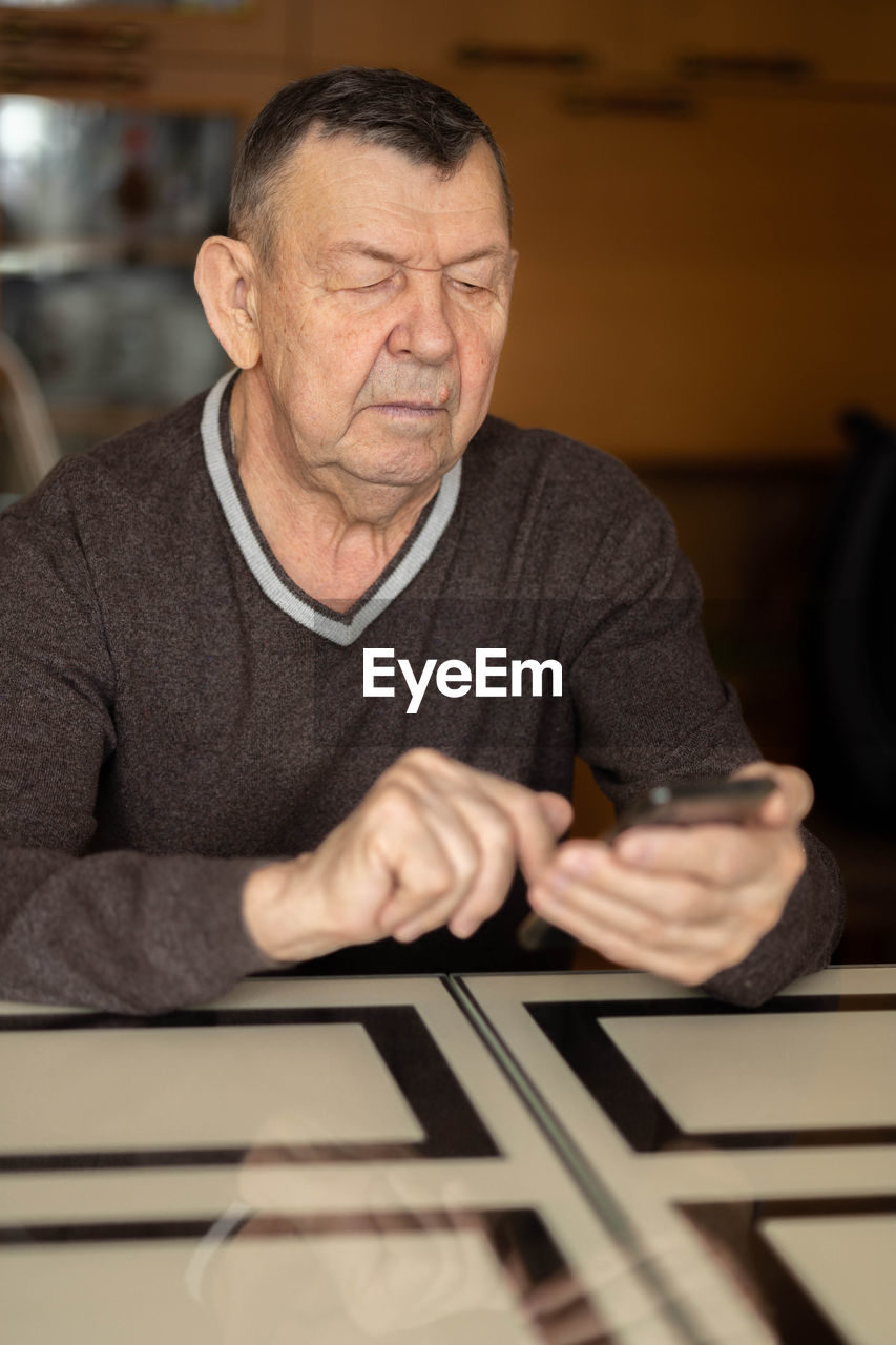 Elderly man dials number in smartphone from home. old senior sends sms on mobile phone