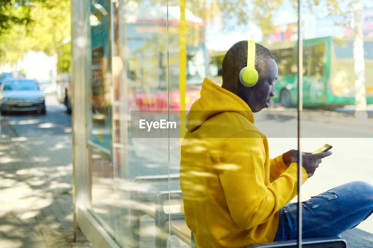 Man listening music while sitting at bus stop