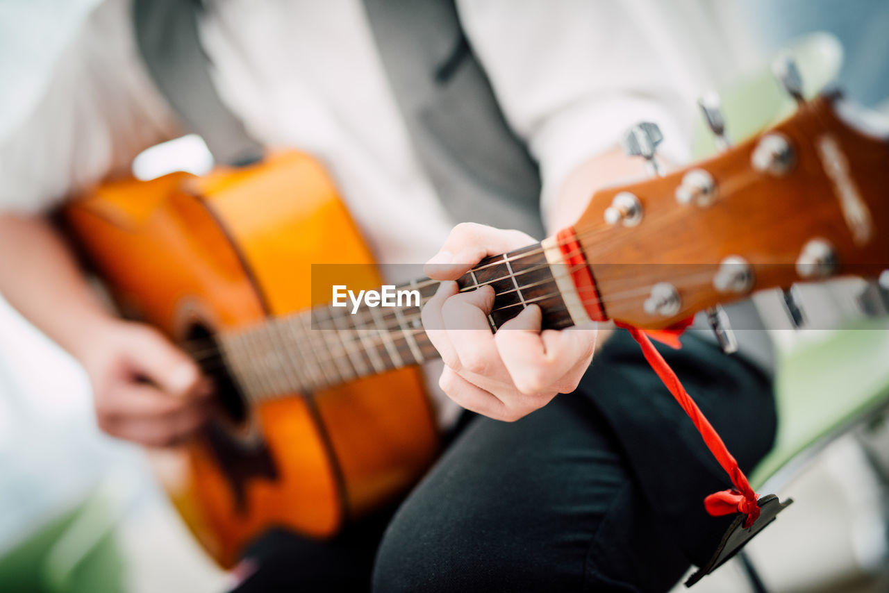 Midsection of male guitarist playing acoustic guitar while sitting on chair