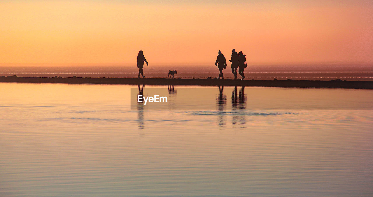 Silhouette people at beach against sky during sunset