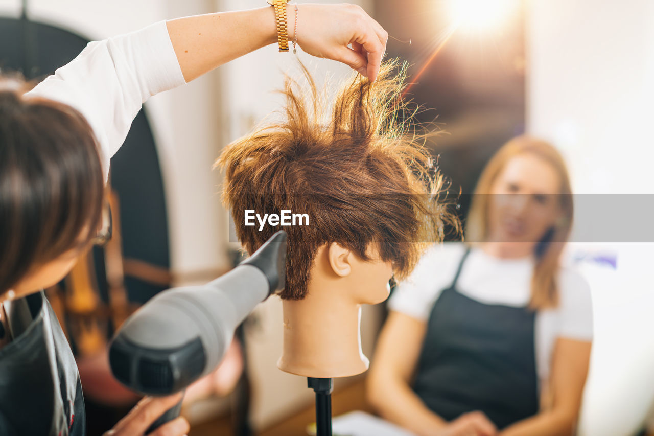 Hairdresser with the hair dryer in hands teaching students how to do hairstyling