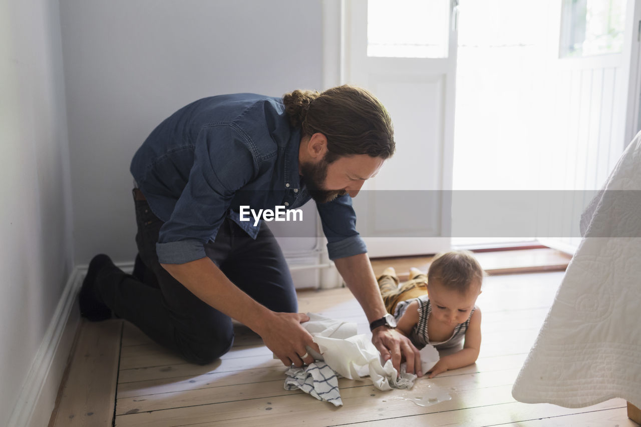 Mid adult father cleaning floor by baby boy at home