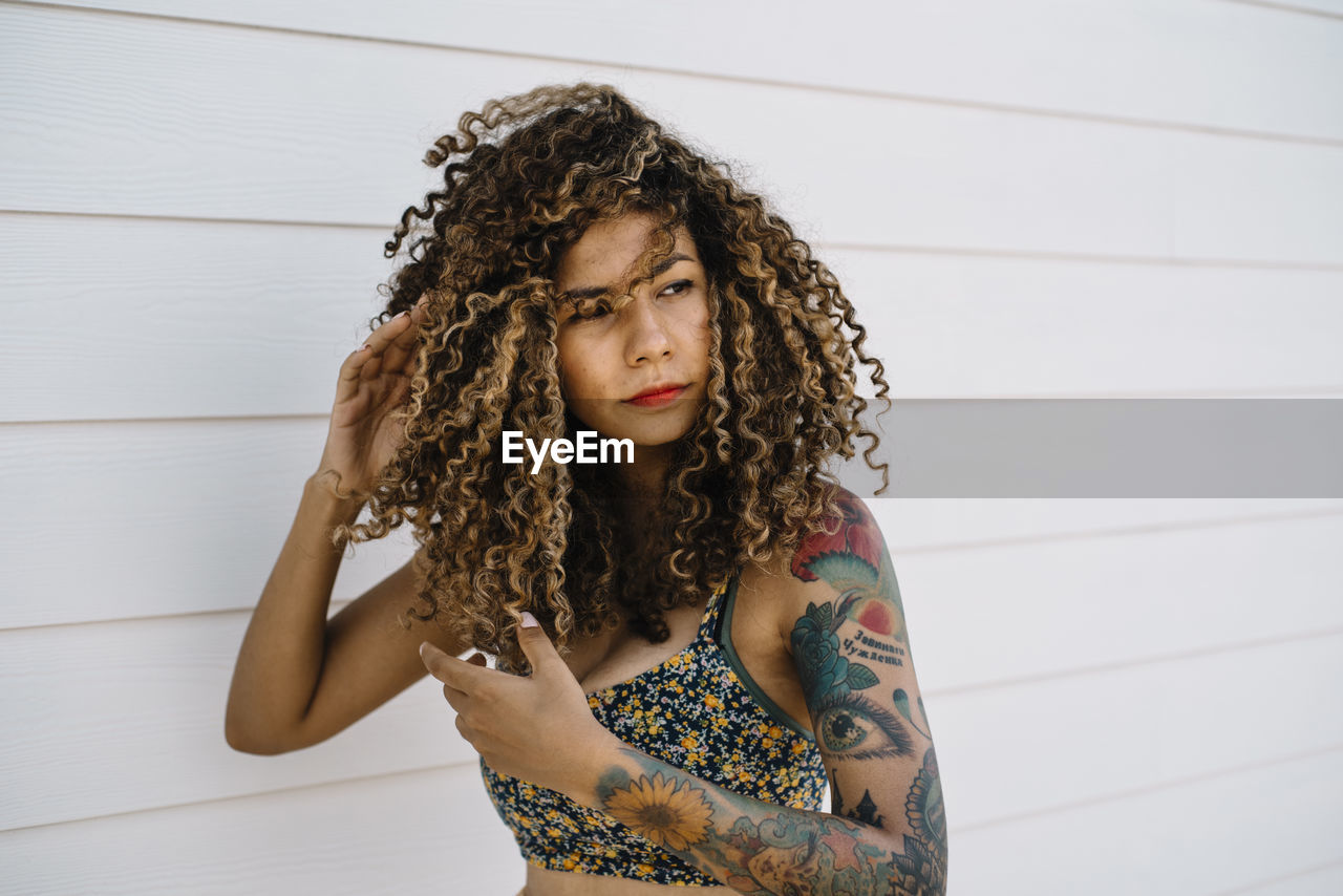 Woman with curly hair standing against wood