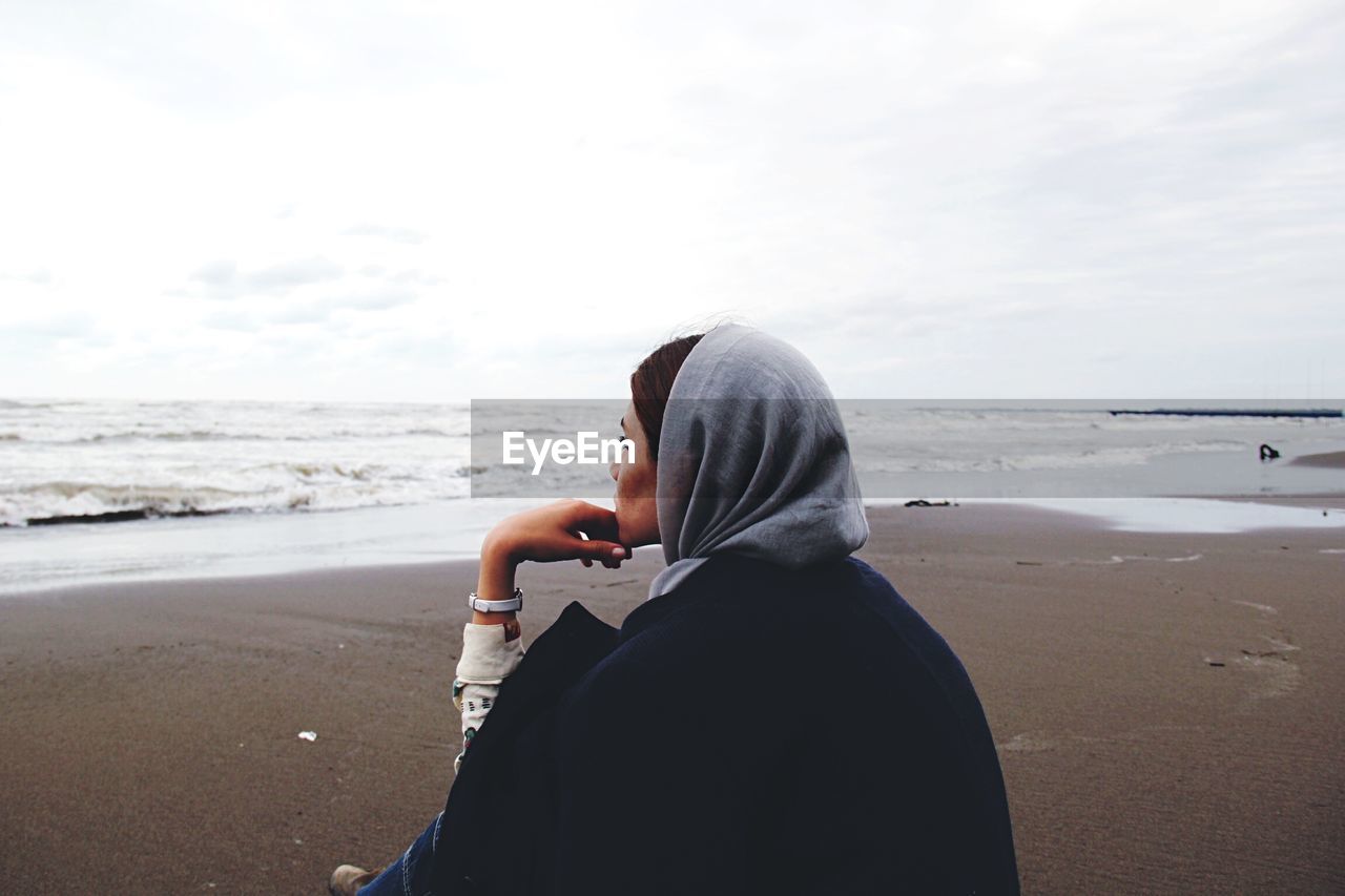 Woman sitting at beach against sky