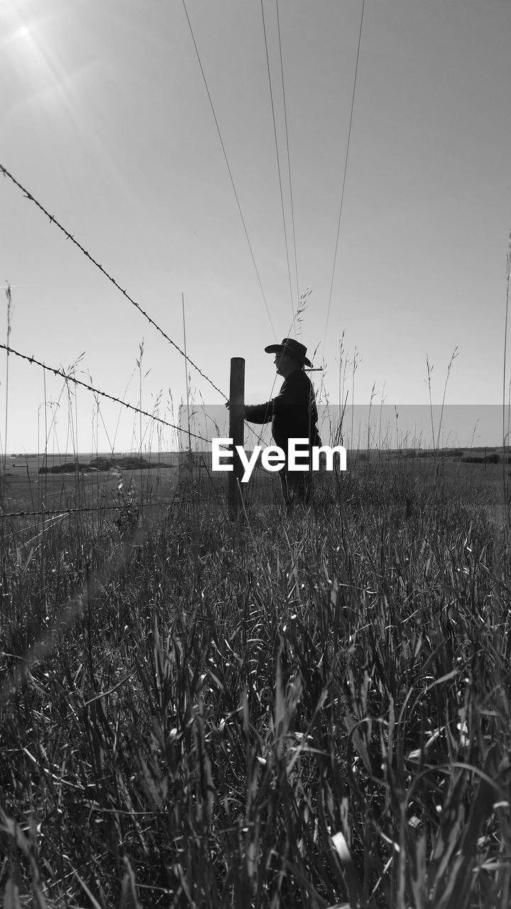 Side view of man standing by fence on land against sky