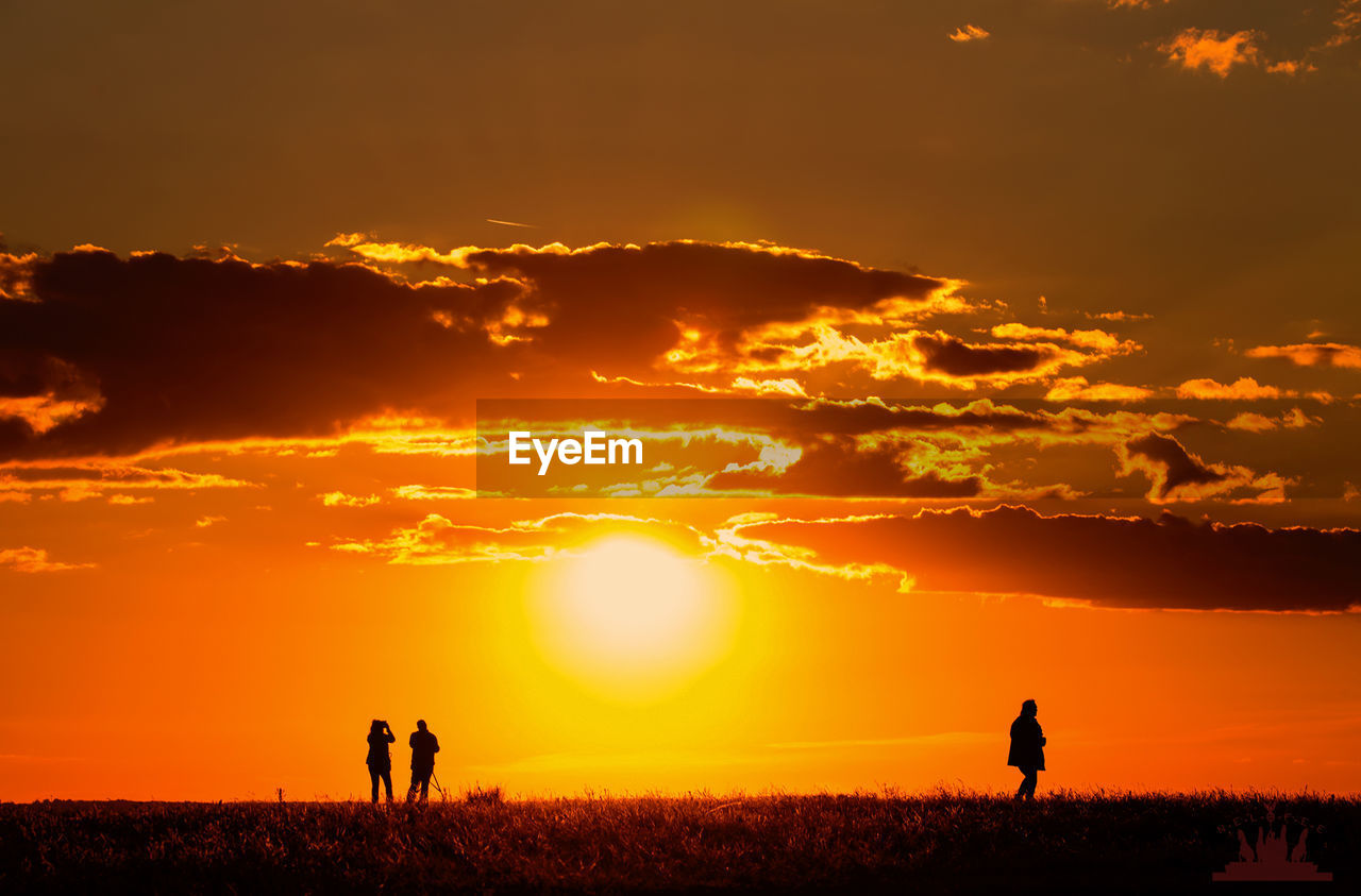 Silhouette people on field against orange sky