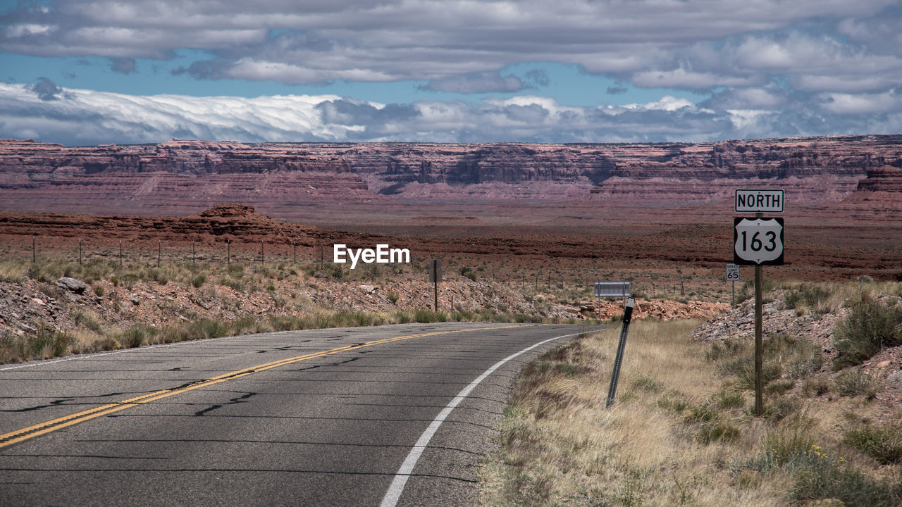 Road sign on landscape against sky